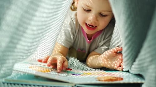 Little Girl Enjoying of Review a Book Under Blue Knitted Plaid in Sunny Morning