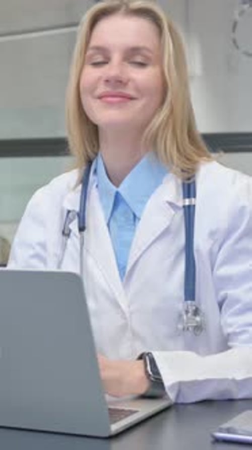 Blonde Woman Doctor Smiling at Computer in Office