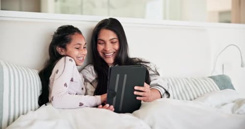 Mother and Daughter Using Tablet in Bed Together