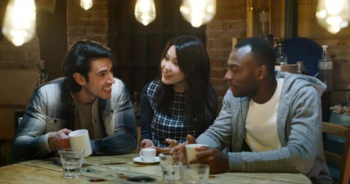 Slow motion of smiling friends having coffee at cafe and having fun with mobile cell phone. Shot i