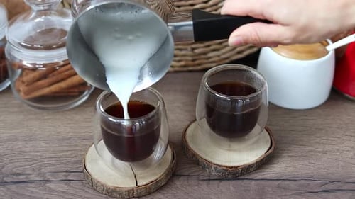 Adding Steamed Milk to Coffee on Wooden Table