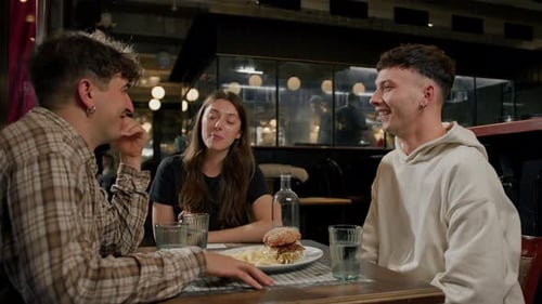 Wide shot - a group of friends chatting at a table in a restaurant, eating a burger and french fries