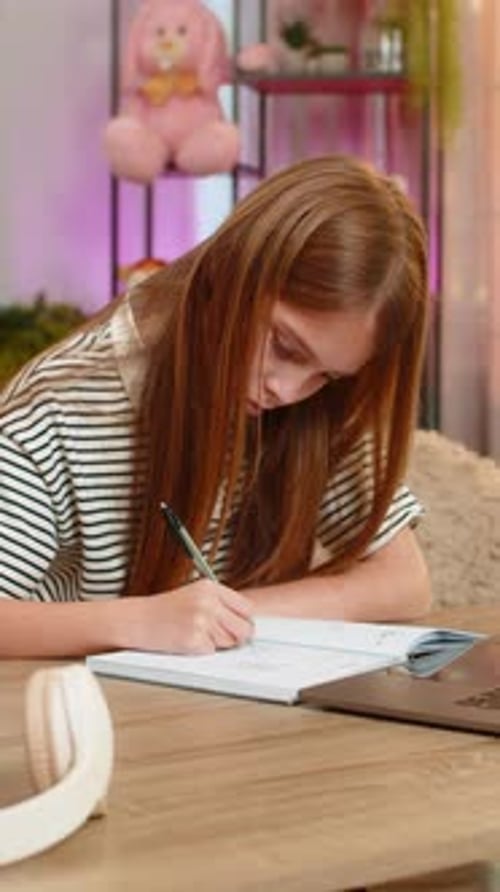 Child Girl Kid Doing Online Homework on Laptop and Writing Math Notes While Sitting at Home Table