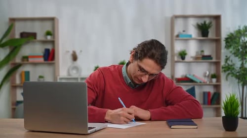 Young Adult Man Spending Time at Home Man Student Sits at Desk Works on Laptop Answering Test
