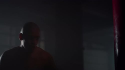 Powerful Man Silhouette Boxer Boxing Punch Bag in Dark Gym. Strong Fighter