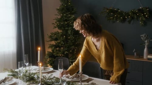 Woman Sets Christmas Table With Candles and Greenery