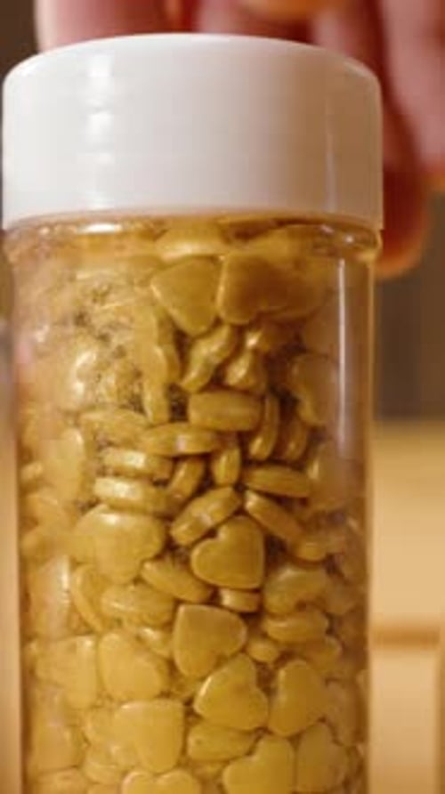 Vertical video. Close-up of a pastry chef examining jars of sugar sprinkles of various shapes.