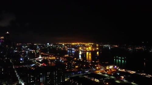Nighttime city skyline with twinkling lights and dark waters reflecting urban glow, high angle
