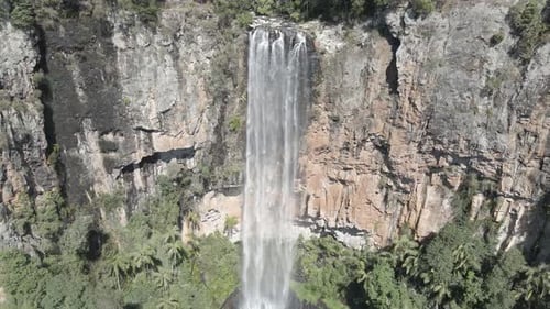 Towering waterfall cascades over rocky cliffs in a dense jungle, mist revealing a radiant rainbow. T