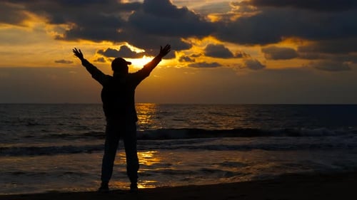Silhouette of a Happy Traveler Raising Hands on the Beach at Sunset