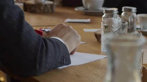 Ein junger Mann im Geschäftsanzug macht sich während eines Geschäftstreffens Notizen. Langsamer Kameraschwenk.