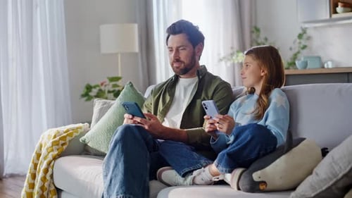 Father and Daughter Relaxing on Sofa Using Smartphones