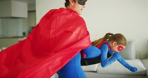 A carefree happy smiling father and daughter dressed as superheroes are having fun to run and jump