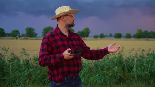Farmer Businessman in Straw Hat Controls Harvesting Using Drone for Observation Combine Harvester in