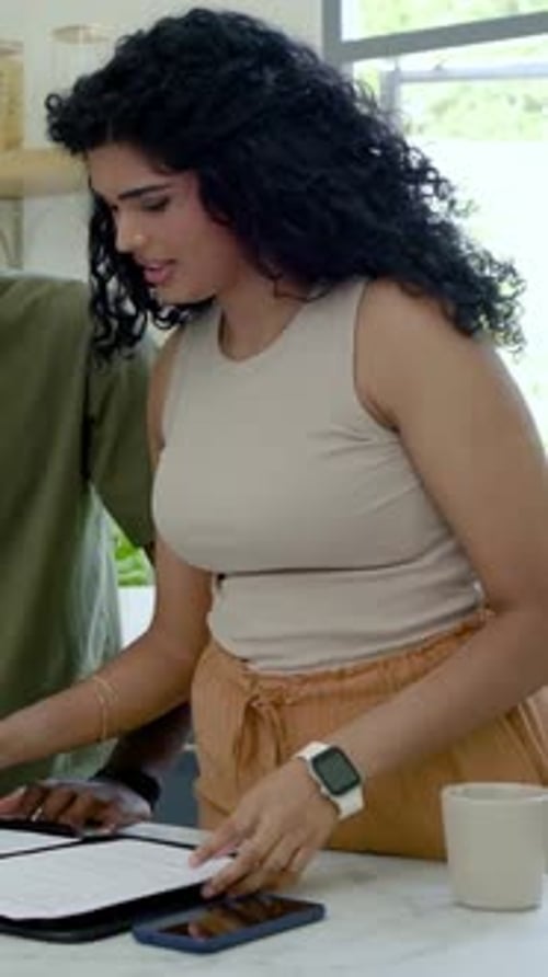 Vidéo verticale : pages étalées, femme en t-shirt beige et homme olive signant des formulaires dans la cuisine, téléphone