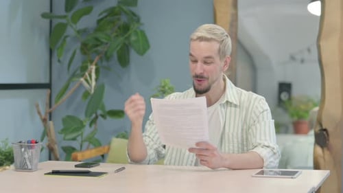Modern Young Man Celebrating Success while Reading Documents in Office