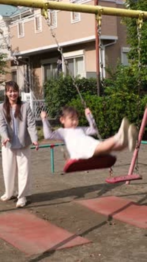 Japanese mother pushing daughter on a swing at the park
