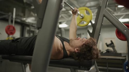 Athletic Man Performing Bench Press Exercise with Barbell in Gym