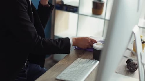 Serious Young Chinese Man with Glasses Uses Computer Speak on Phone Write in Notebook Office
