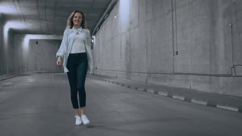 Happy Beautiful Cool Young Blond Woman is Walking in a Lit Concrete Tunnel. She's Wearing a Striped
