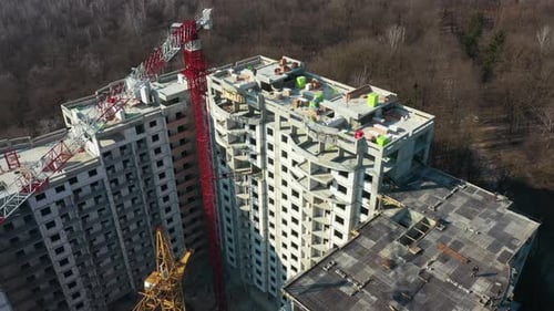 Flying around. Aerial view of construction of a multi-storey building. People working on the top