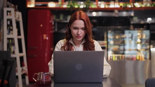 Serious Woman Working on Laptop at Cafe Table While Sitting Upright Concentrating on Screen Writing