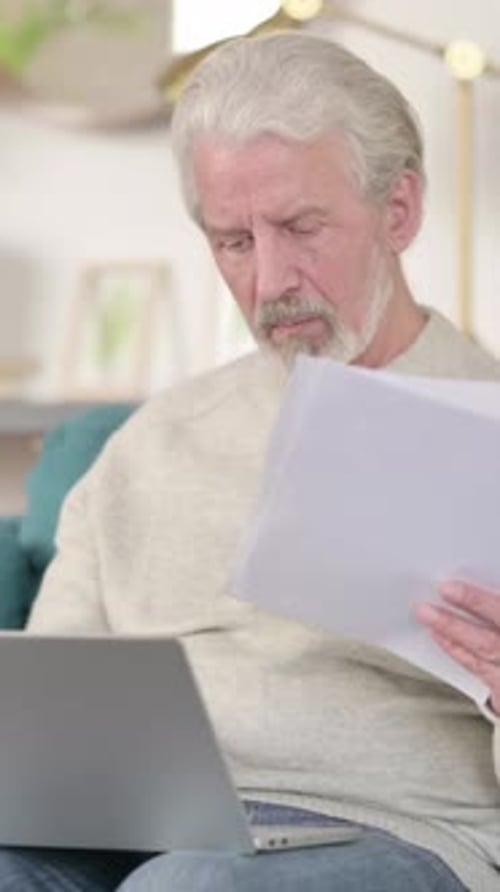 Senior Man Reviews Documents While Working on Laptop
