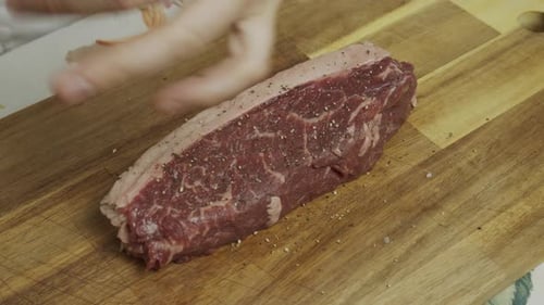 Adding spice onto meat steak on cutting board. Slow motion close up shot.