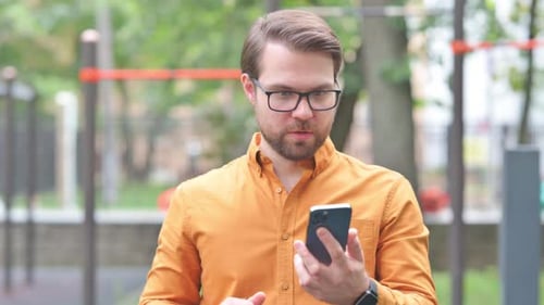 Man Using Smartphone Reacts with Success Outside