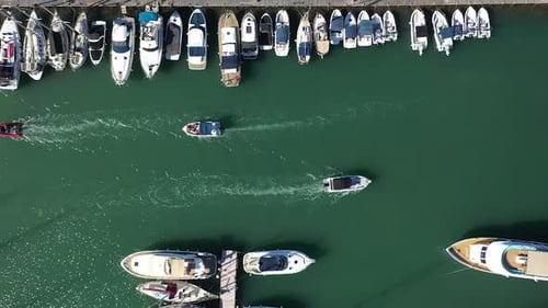 Boat traffic in a Latchi port passing moored yachts, aerial downwards view