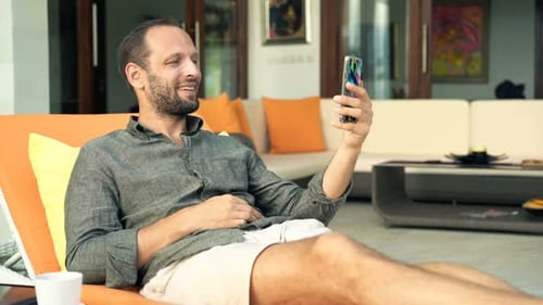 Man Relaxing on Lounge Chair Using Smartphone