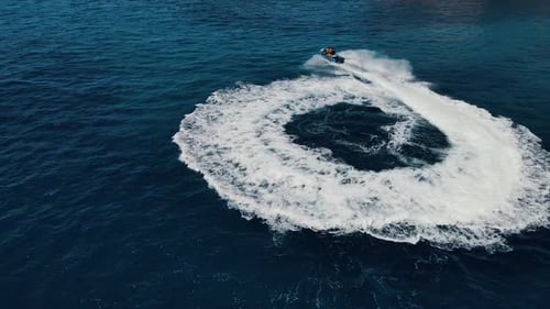 Two people are riding water scooter, jet ski, making circles and rotating moves on water surface, at