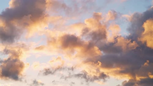 Golden red light illuminates soft fluffy clouds in the sky at sunset