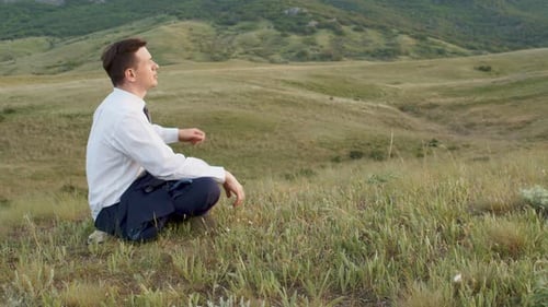 Erwachsener junger Mann im Business-Anzug im Profil inmitten der Hügel in entspannter Pose und Blick auf den Sonnenuntergang