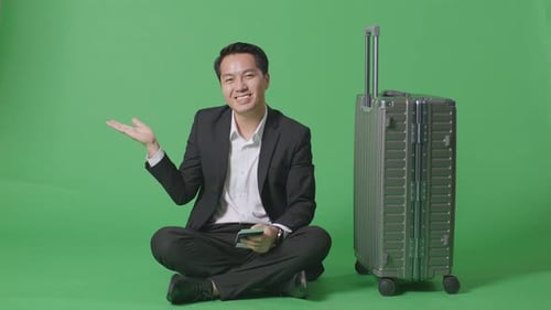 Businessman With Luggage And Passport Smiling And Pointing To Side While Sitting In The Green Screen