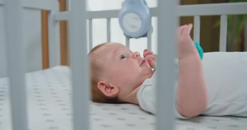 Portrait of a playful little baby is smiling cheerfully through the sides of the crib. Joyful lovely