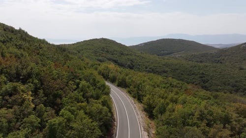 Croatia, a road through mountains covered with green forest, aerial view.
