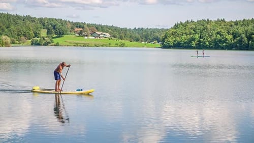 A tall man paddles on stand up paddle boards (SUP) on a river in the sunshine, having fun and smilin