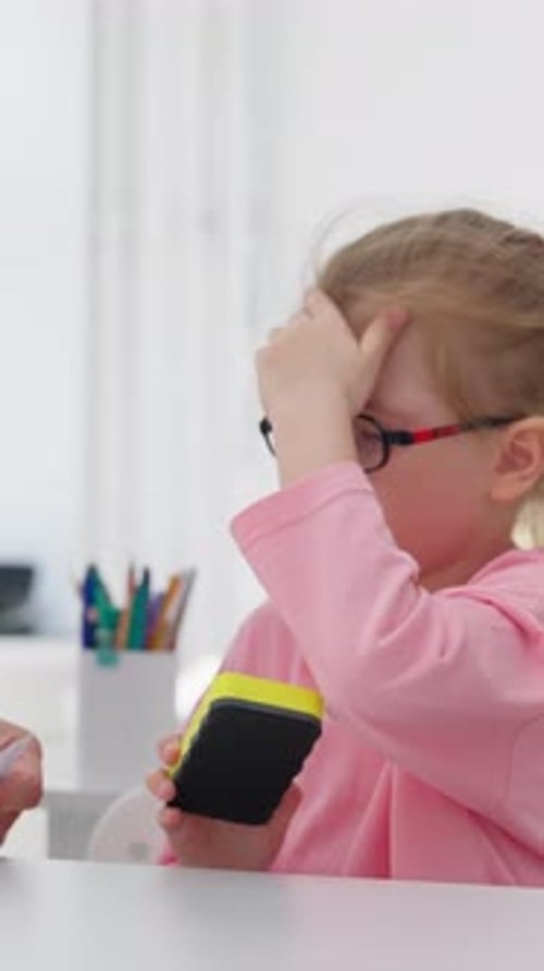 Young Girl in Pink Thinking at Desk Holding Sponge