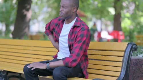 Man Rubbing Lower Back in Park