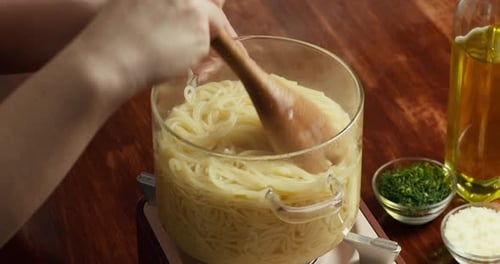 Closeup of Hands Mixing Cooked Spaghetti in Pot with Wooden Spoon on Wooden Table Homemade Pasta