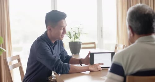 Young Adult Explains Tablet to Senior at Table