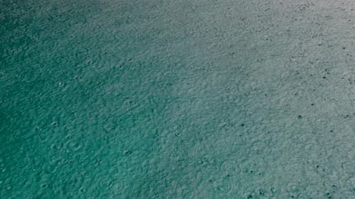 Close up of raindrops during rain downpour onto turquoise ocean water