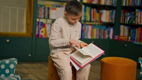 in Bookstore in the Children Area a Handsome Little Boy in Light Clothes Reads a Book