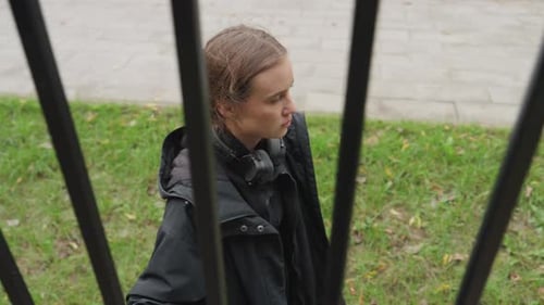 Pensive Young Woman Behind Metal Bars in Urban Setting
