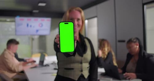 Empresária sorri para a tela do smartphone e estende o dispositivo de tela verde em direção à câmera,