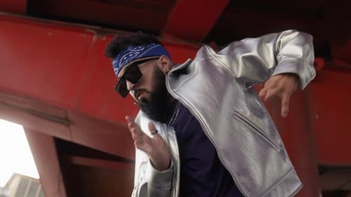 Homem de hip hop com bandana, óculos escuros e jaqueta se exibindo na rua da cidade