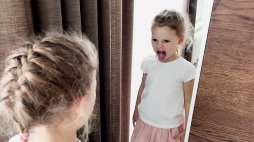 Kleines blondes Mädchen lächelt über ihr Spiegelbild Kind verzieht vor einem Spiegel das Gesicht