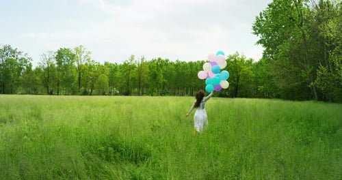 Happy Woman Running with Balloons in Grassy Field