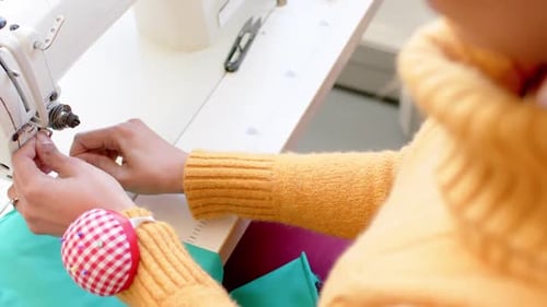 Biracial female fashion designer threading sewing machine in studio, slow motion